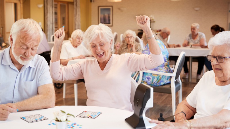 Tre glada seniorer vid ett bord spelar bingo.